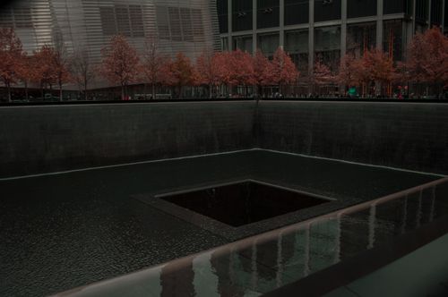 Free Somber view of the 9/11 Memorial Pool with autumn trees and urban backdrop. Stock Photo