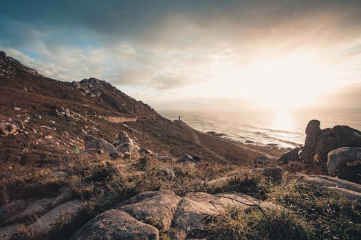 俯瞰崎岖的海岸线，岩石与远处的灯塔点缀其间，日落景色令人惊叹