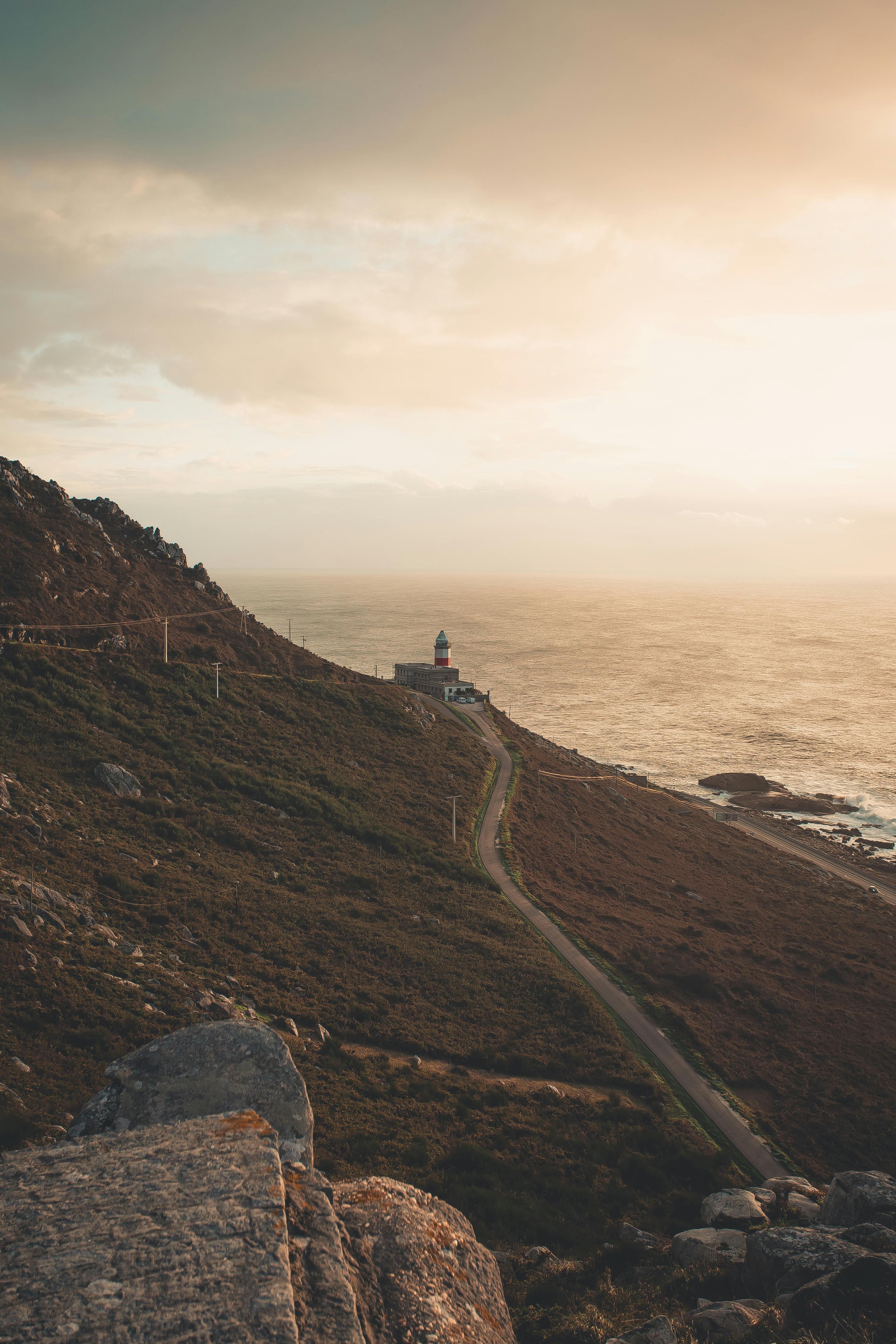 日落时分，海边灯塔、崎岖的悬崖与宁静的大海构成了一幅壮丽的景色