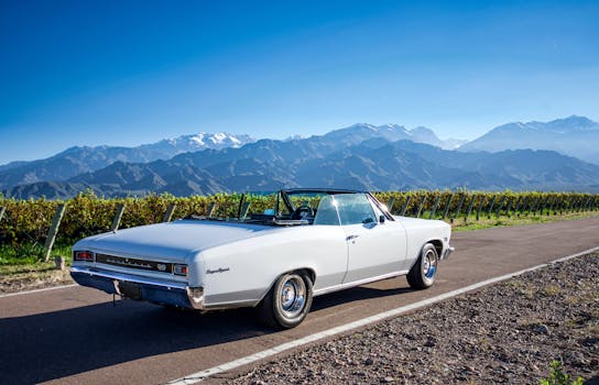 Vintage white convertible car driving along a vineyard road with stunning Andes mountain views in Tunuyán, Argentina.