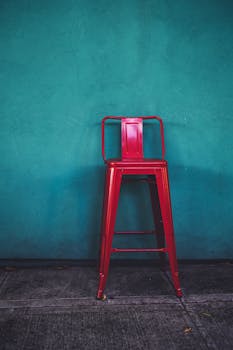 在俄勒冈州波特兰市的一处城市户外环境中，一把引人注目的红色金属凳靠在充满活力的青色墙壁上