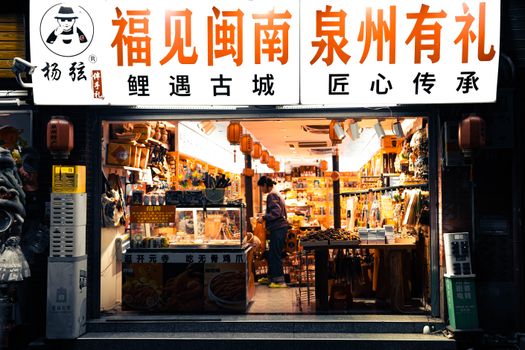 A bustling shopfront in a street market in Quanzhou, vividly lit and filled with local goods and lanterns.