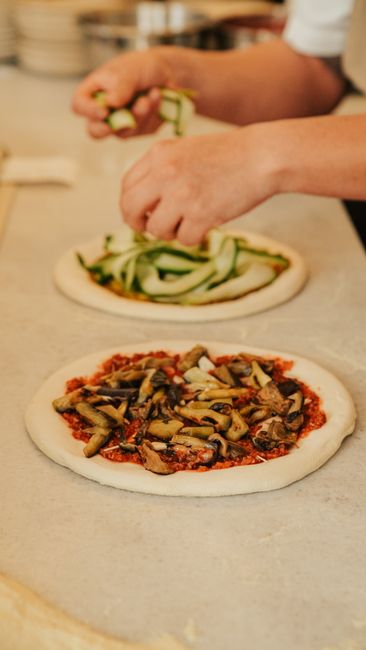 Fotomural El chef añade calabacín fresco a la masa de pizza hecha a mano, mostrando el arte culinario.