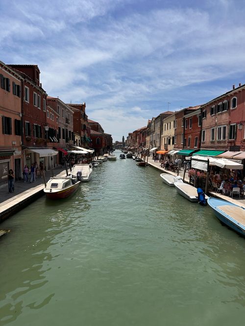 Free Picturesque view of a Venetian canal with boats, colorful buildings, and blue sky. Stock Photo