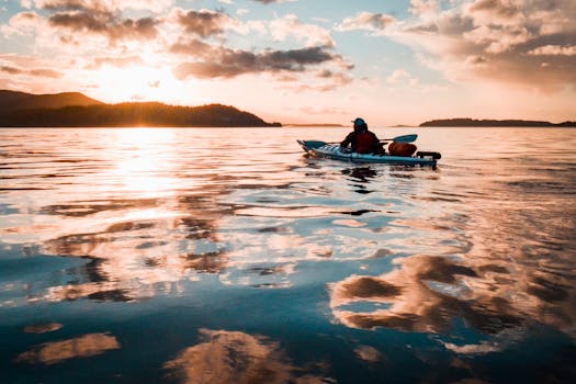 A kayaker paddles during a serene sunset on Vancouver Island, reflecting vibrant colors on the water.