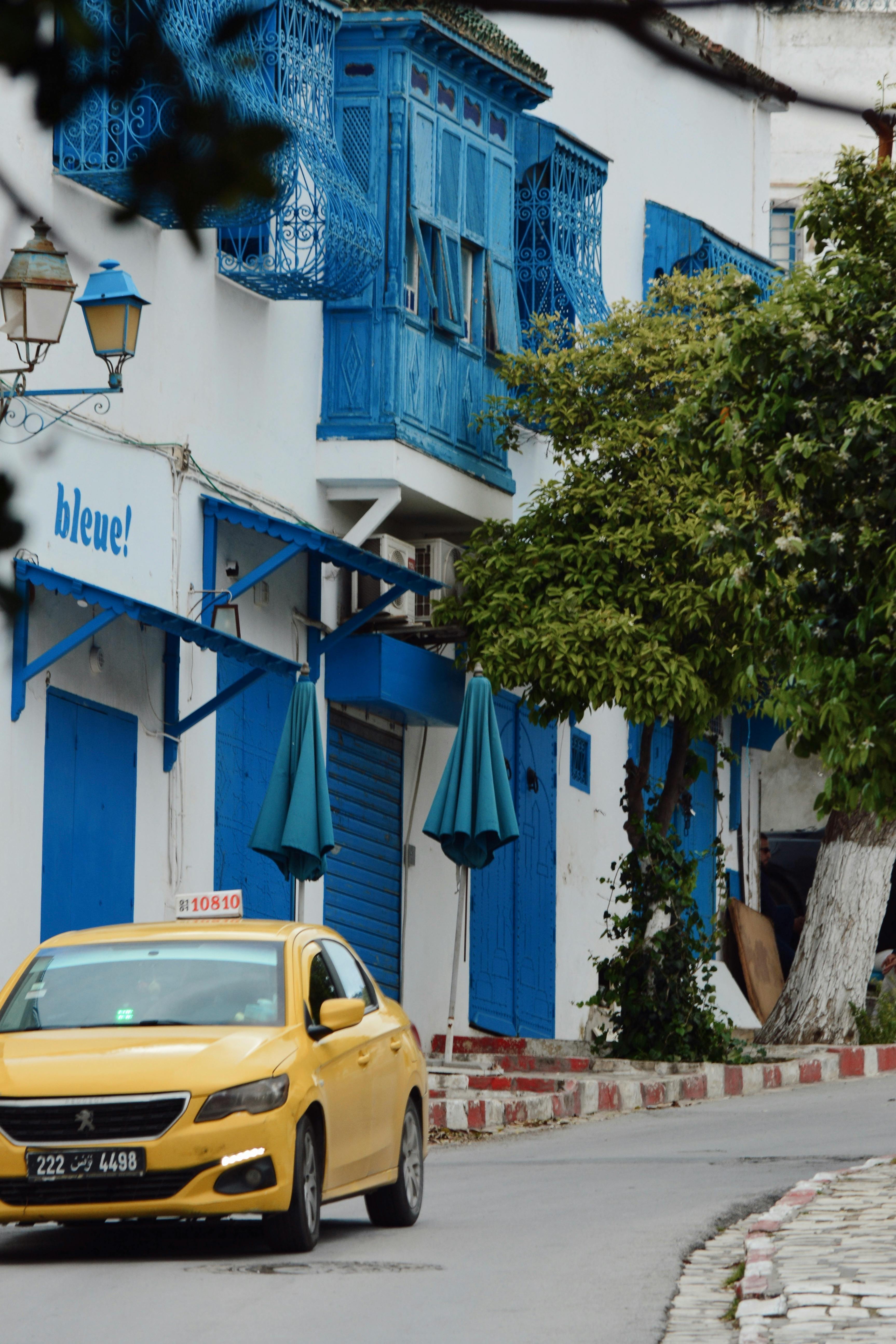 Vibrant blue buildings line a picturesque street in Sidi Bou Said with a yellow taxi passing by.