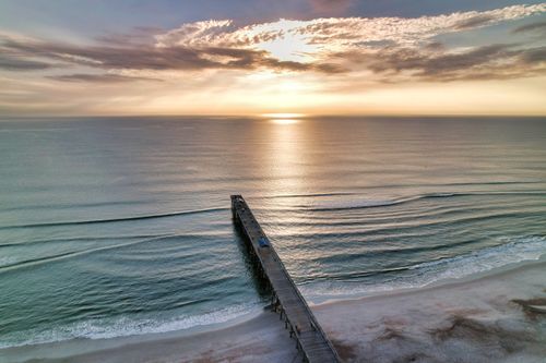 Free A tranquil sunset over a pier extending into the calm ocean waves. Stock Photo