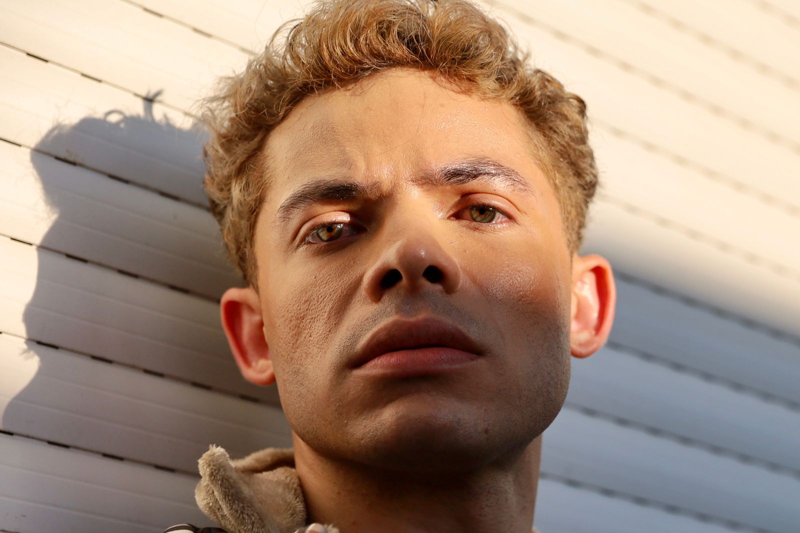 Face turned up into low afternoon sun against a clapboard wall, from a documentary still. Photo by Flávia Vicentini on Pexels