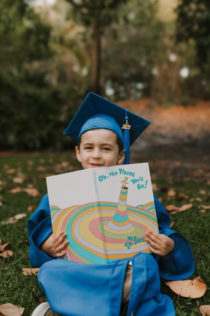Child in blue graduation gown and cap holds Dr. Seuss book in Delray Beach, FL.