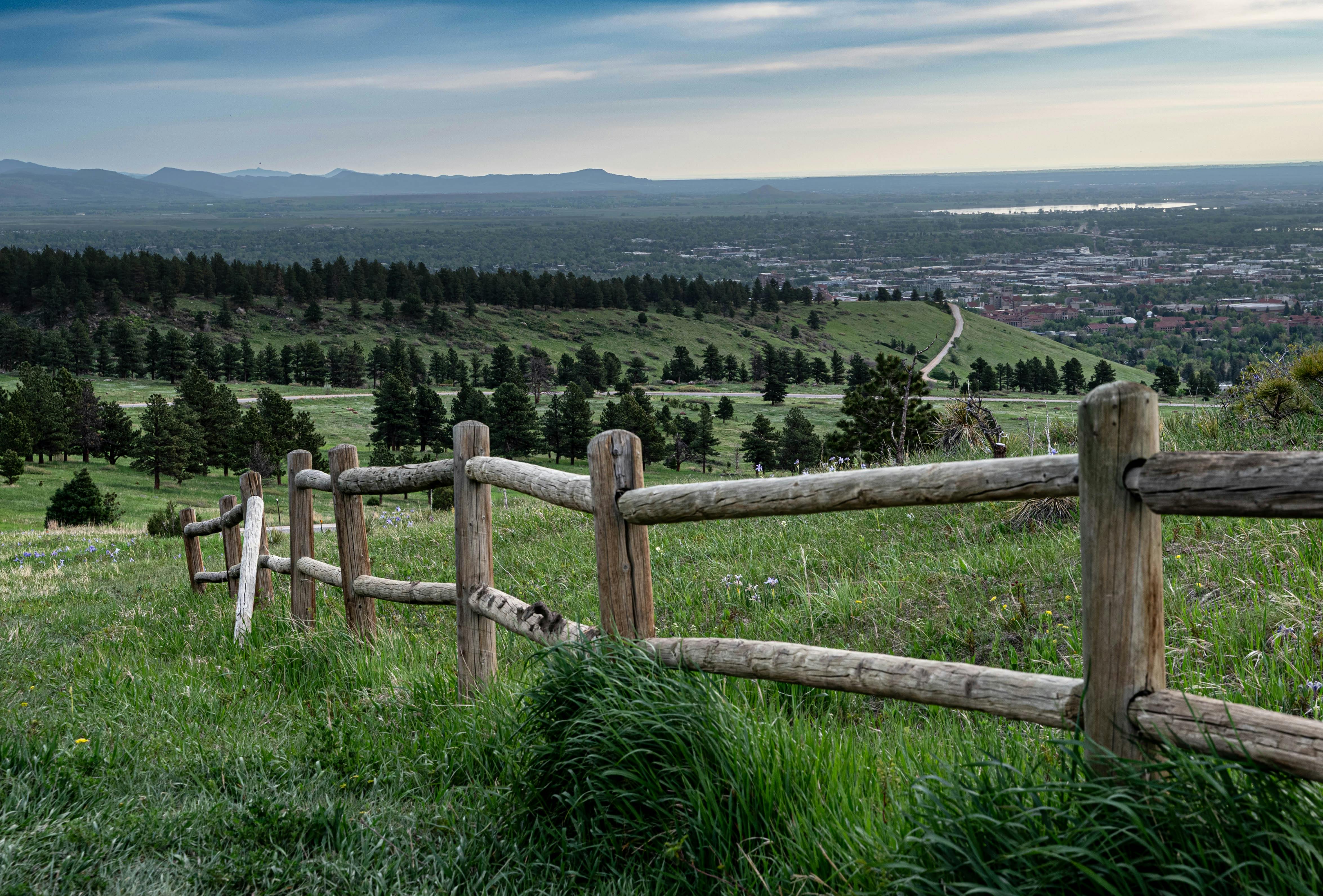 A breathtaking view of a rural area with a wooden fence in the foreground and lush greenery spread across the horizon.