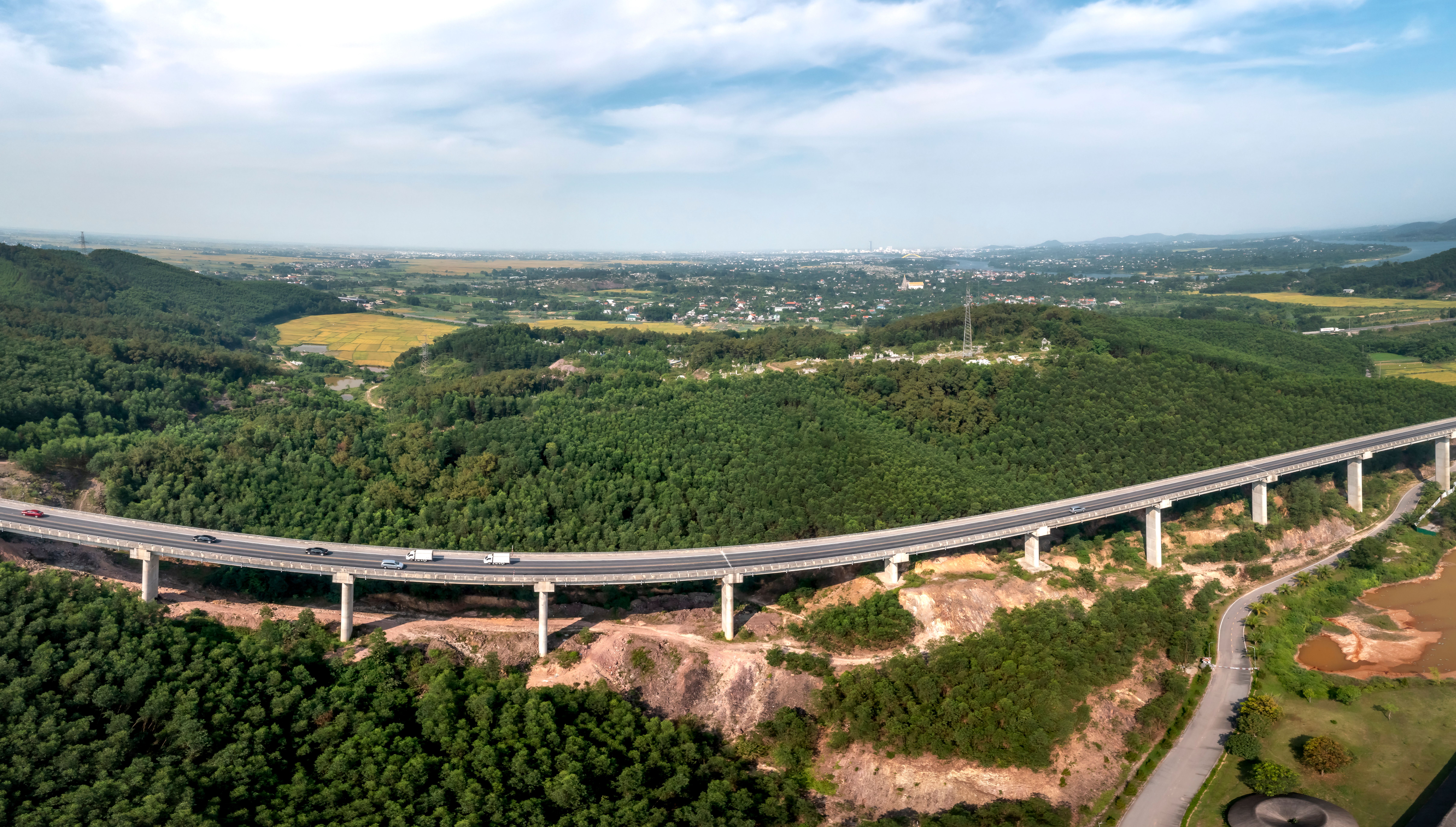 Aerial view of a highway curving through lush green hills under a blue sky.