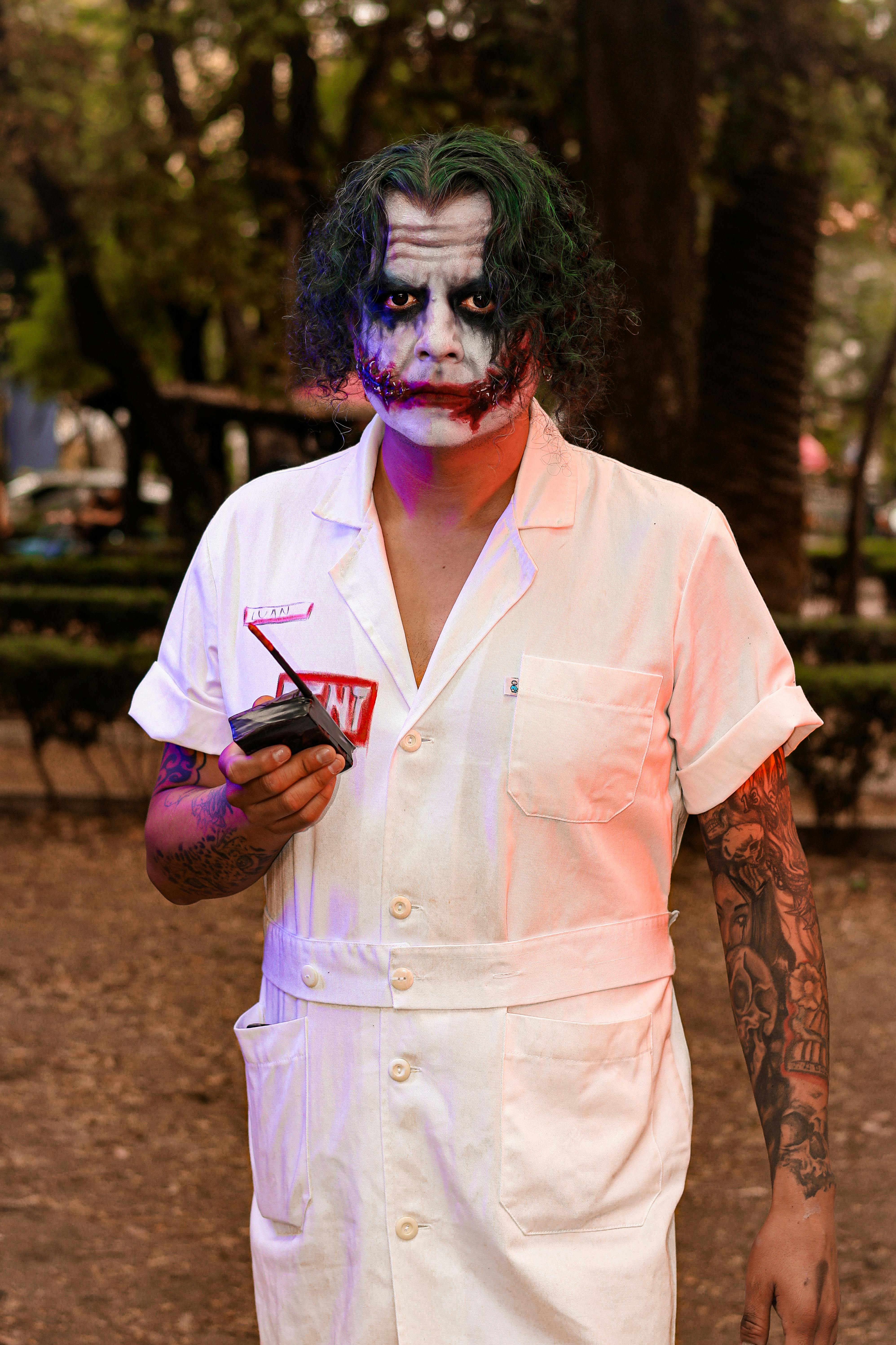 Person in Joker costume and makeup holding a detonator outdoors.