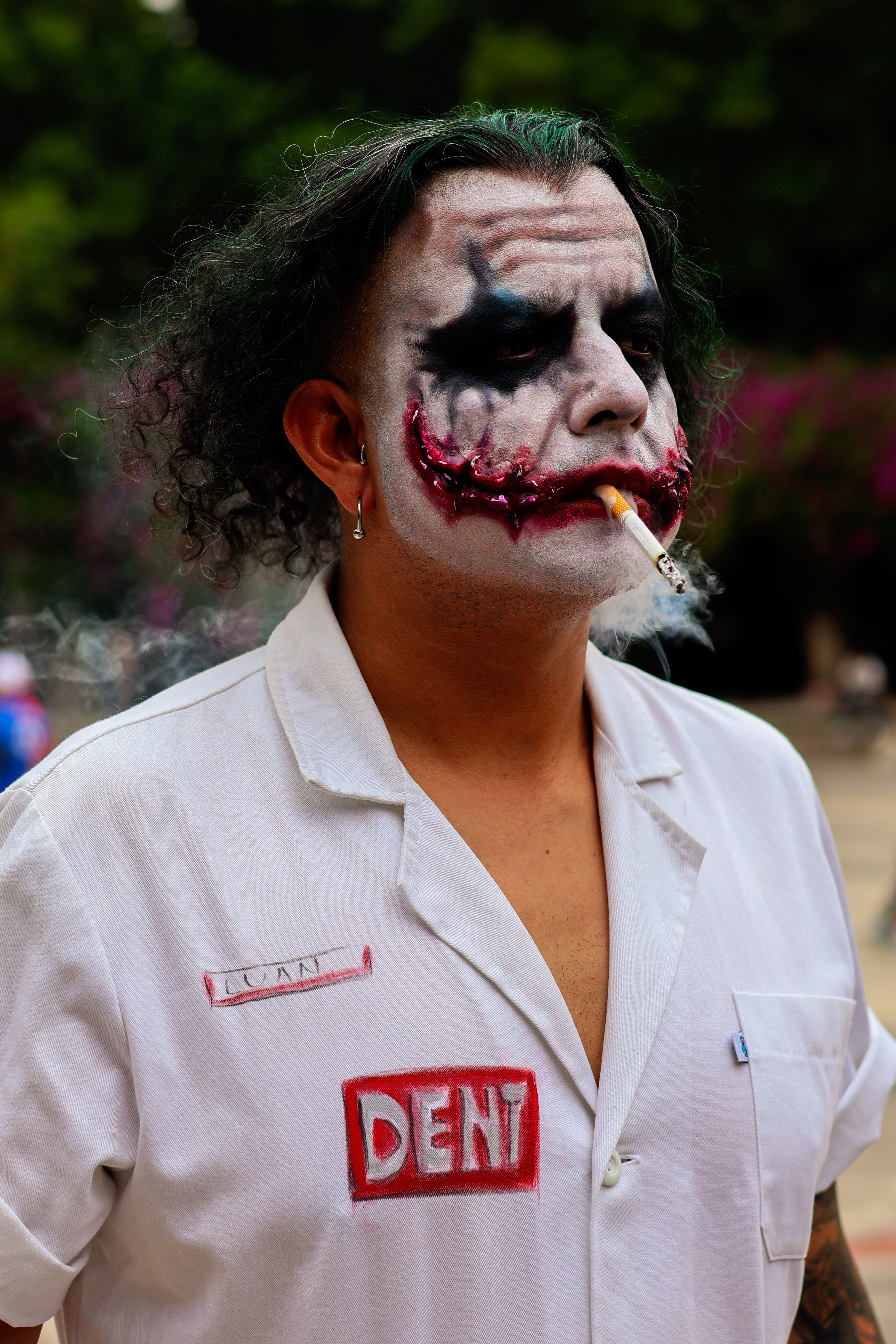 A person in Joker cosplay with dramatic makeup and costume outside, holding a cigarette.