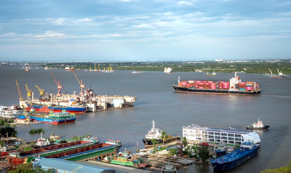 A busy shipping port with cargo ships and cranes under a clear sky, viewed from above.