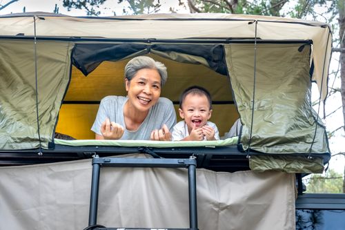 Free Smiling grandmother with child in a rooftop tent during a joyful camping trip. Stock Photo