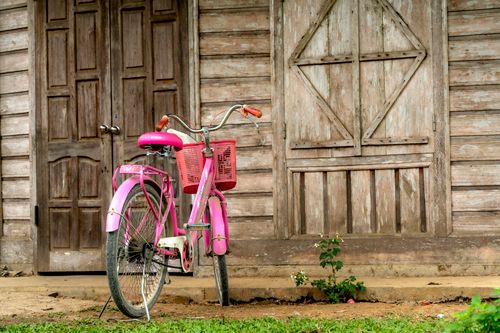 Free Vintage pink bicycle leaning against rustic wooden house wall. Outdoors scene. Stock Photo