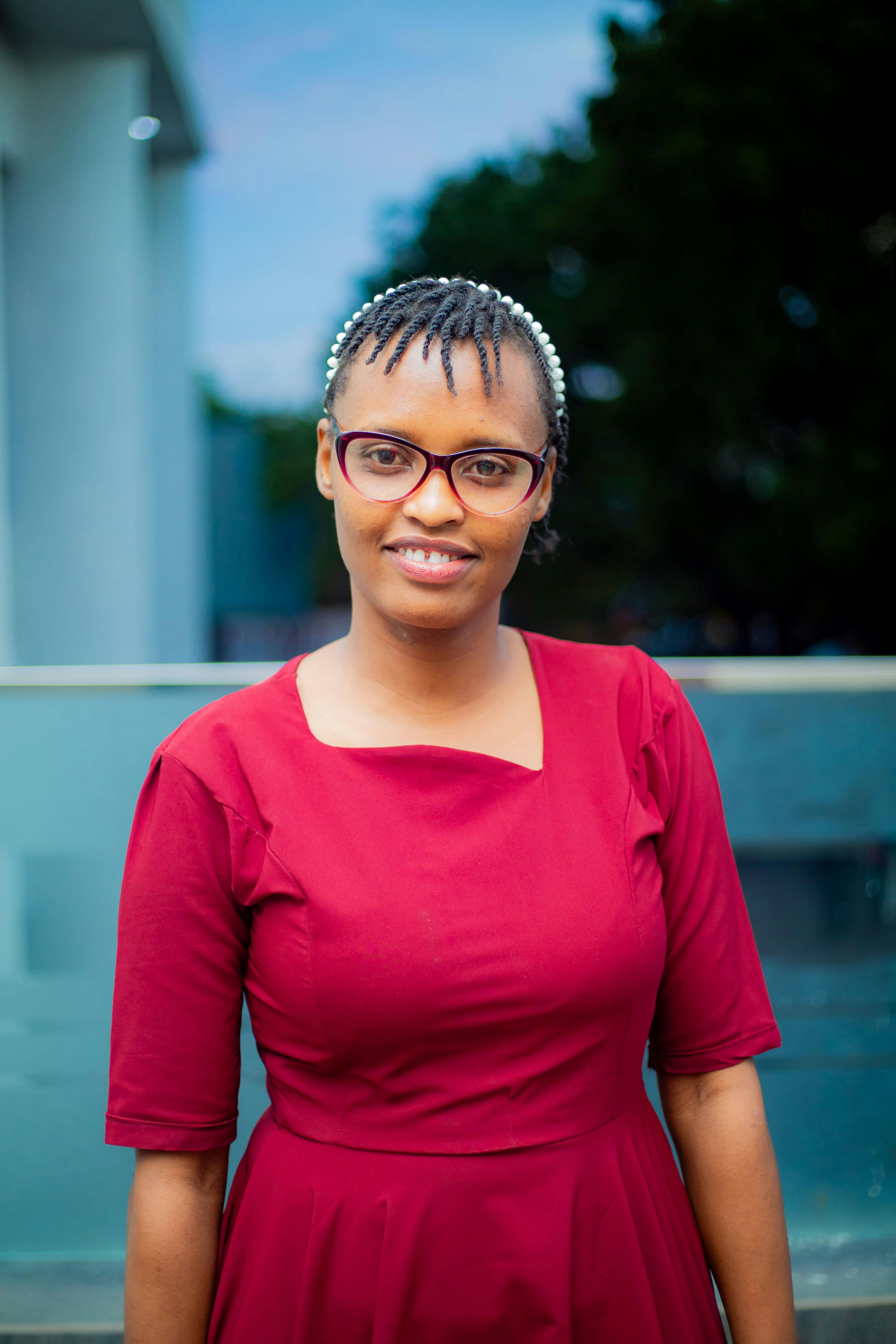 A portrait of a smiling woman in a red dress with glasses standing outdoors.