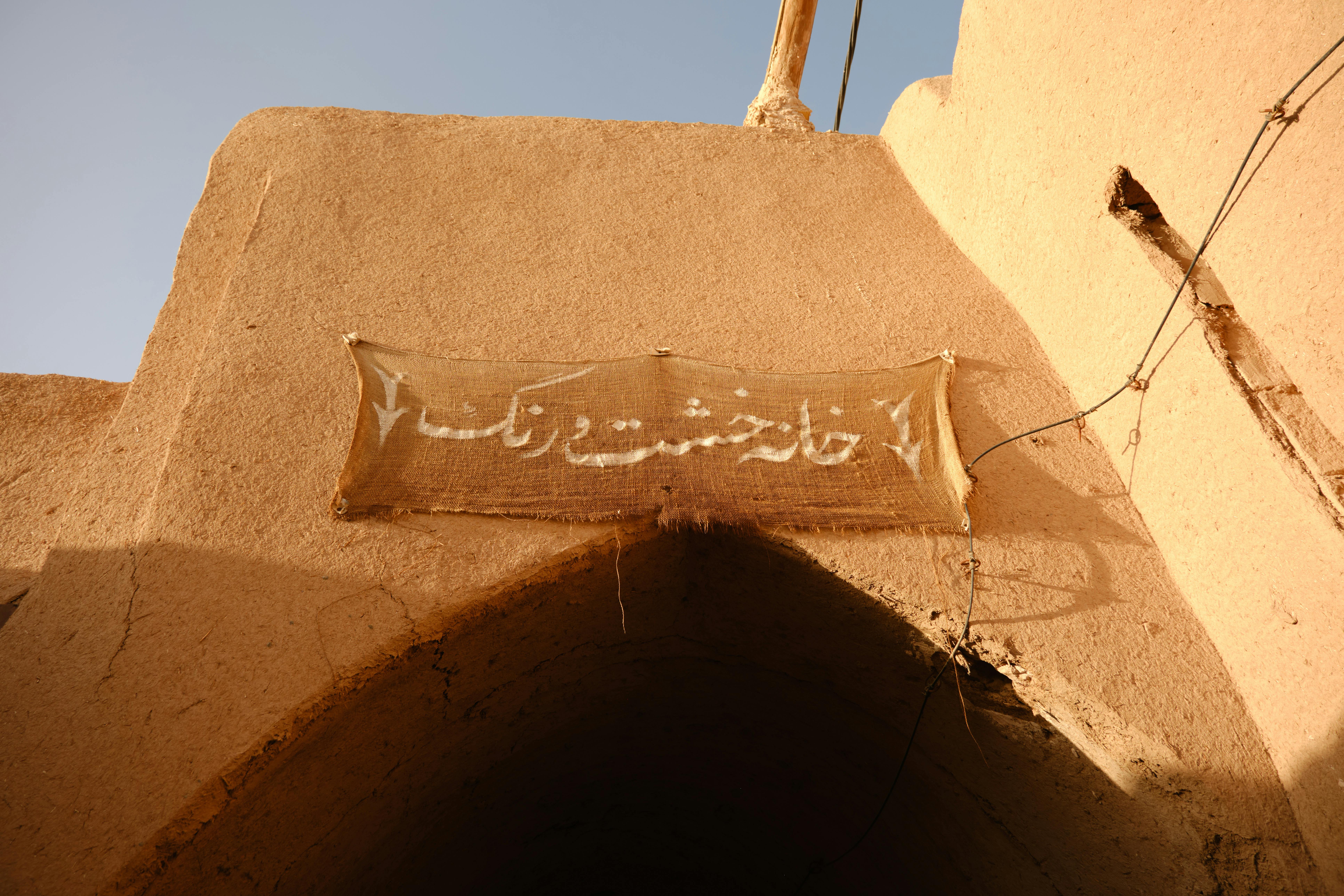 A rustic textile sign hangs over a historic clay archway basking in warm sunlight.