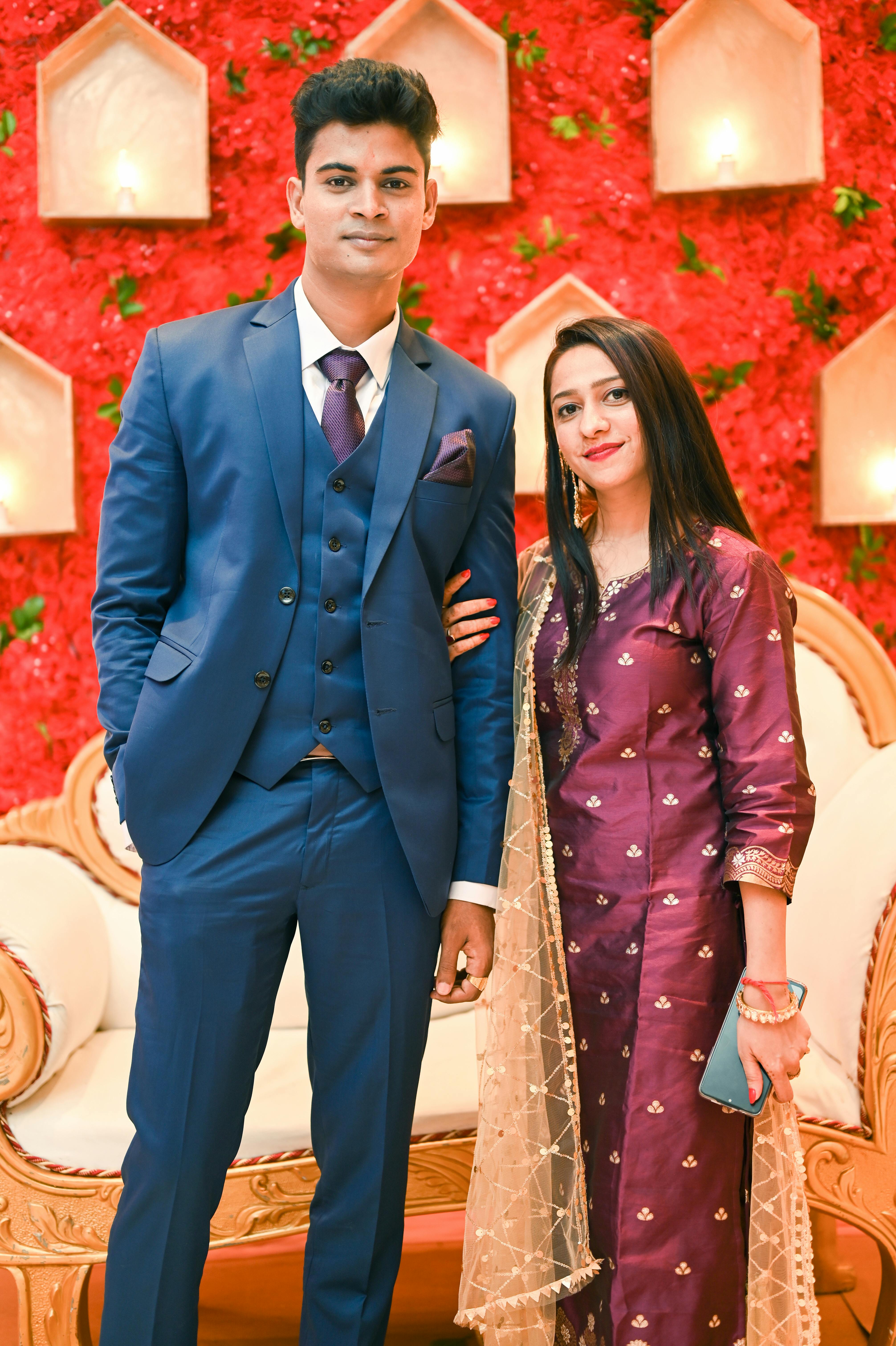 A couple elegantly dressed, posing at a vibrant wedding setting with red floral decor.
