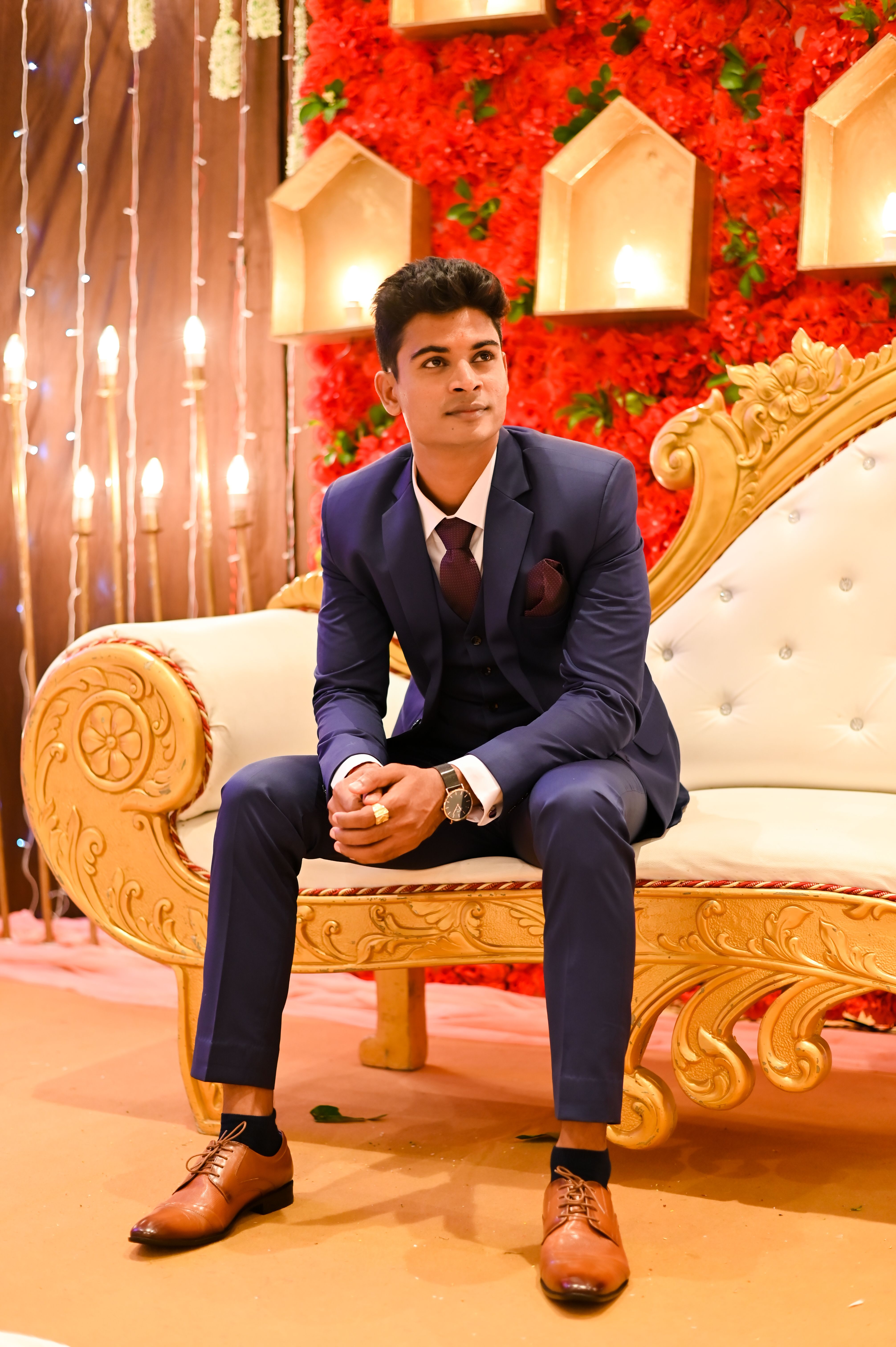 Stylish groom in blue suit seated in lavish wedding setting, exuding elegance.