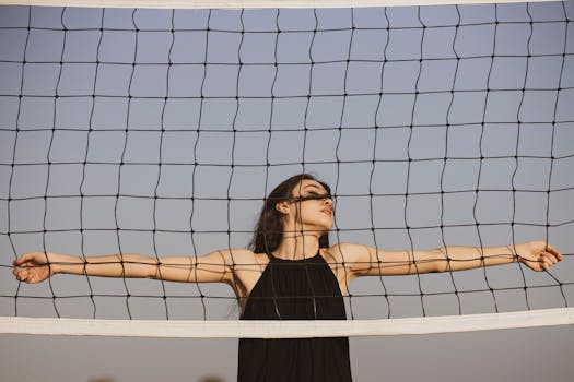 一位身着黑色连衣裙的时尚女子，在晴朗的蓝天下，于排球网后优雅地摆出姿势