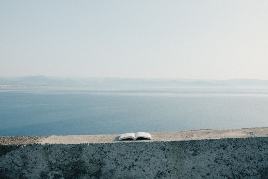 A solitary open book rests on a ledge with a serene sea view and clear skies.
