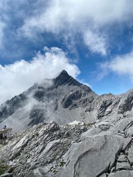Dramatic mountain landscape with rocky peaks and clouds under a blue sky.