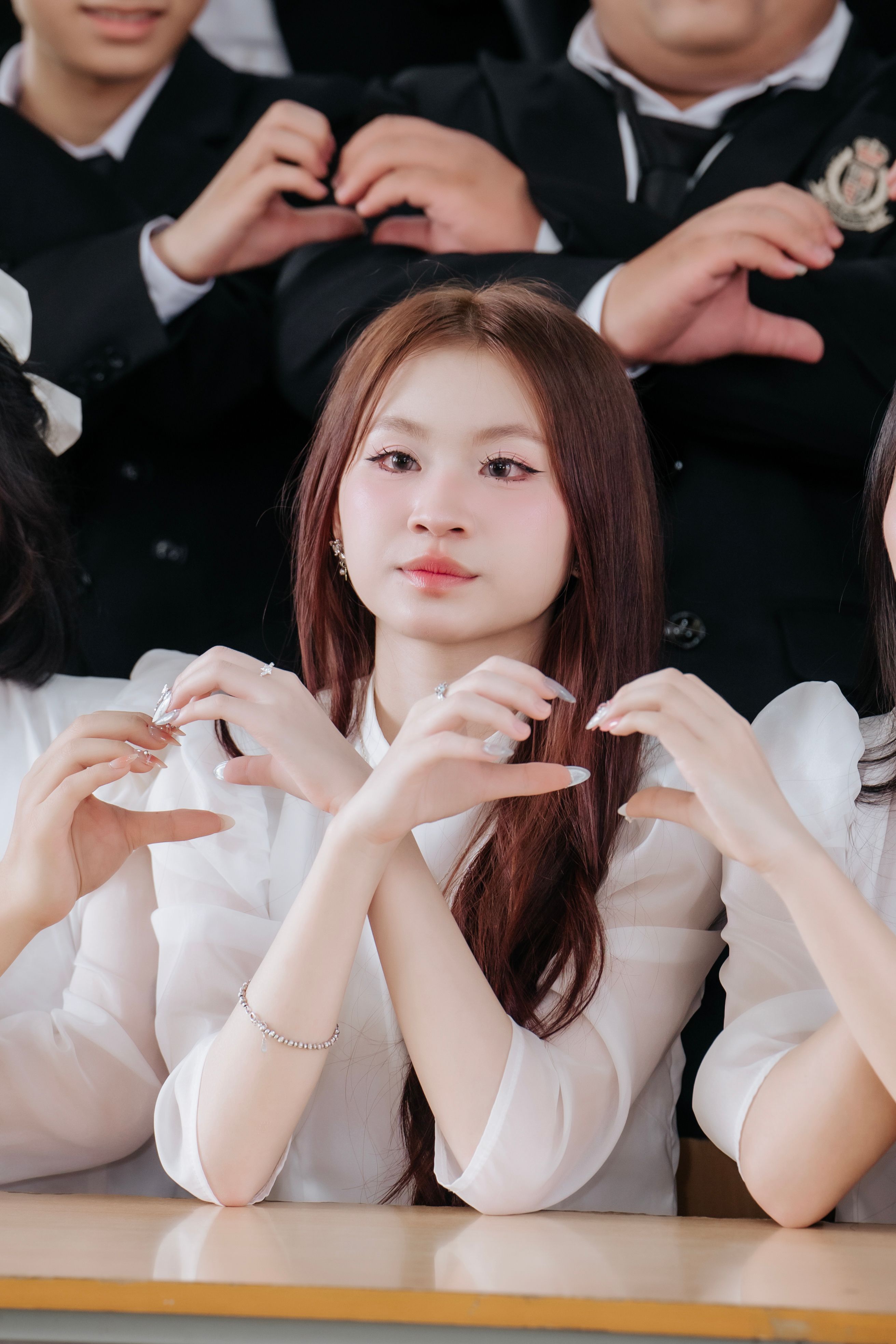Group of young adults in white clothing forming heart shapes with hands indoors.
