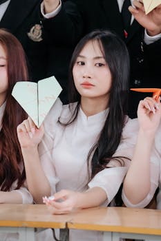 Focused young woman in classroom holding paper airplane, expressing creativity.