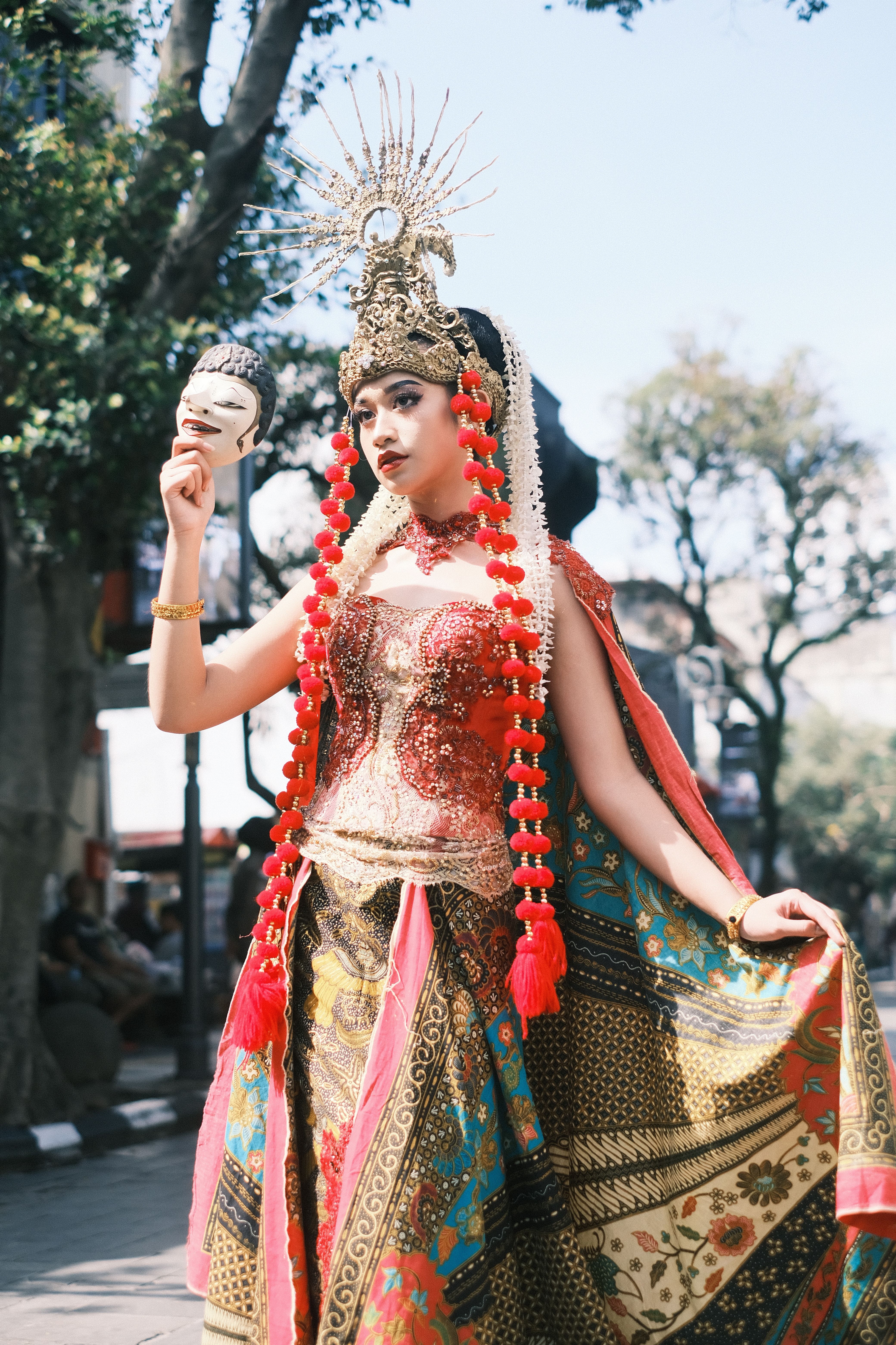 Traditional Indonesian dancer in vibrant attire holding a mask outdoors in West Java.