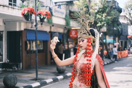 Free A traditional dancer in ornate costume and headdress holds a mask in West Java, Indonesia street. Stock Photo