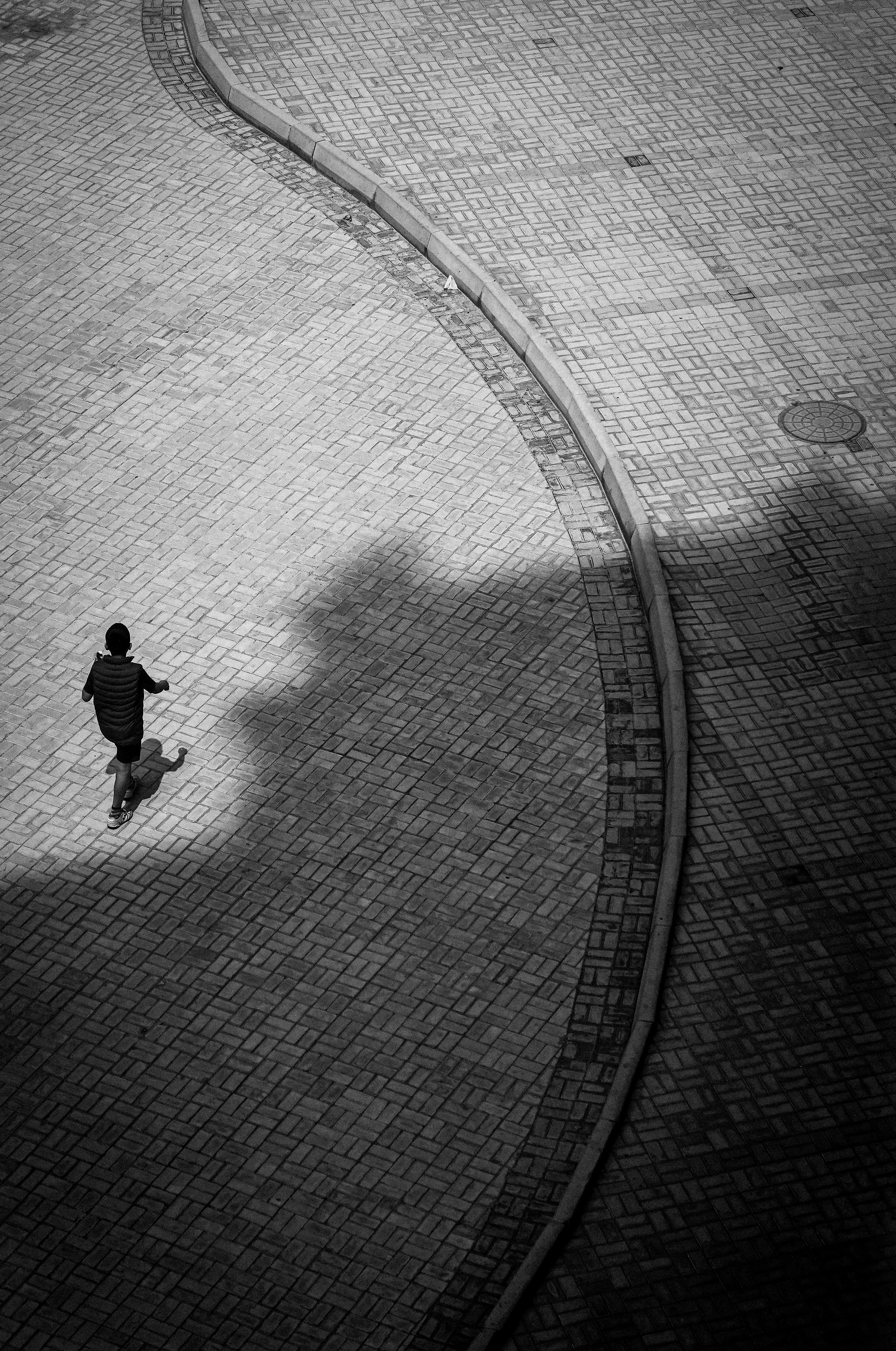 A lone figure walks on a winding cobblestone path, casting a shadow.