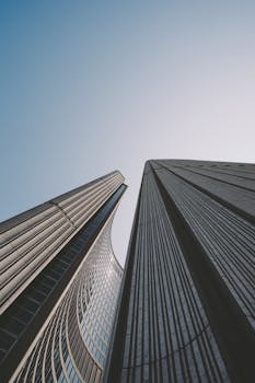 从低角度仰视高耸的现代摩天大楼，背景是简约无云的天空，展现了城市建筑的魅力