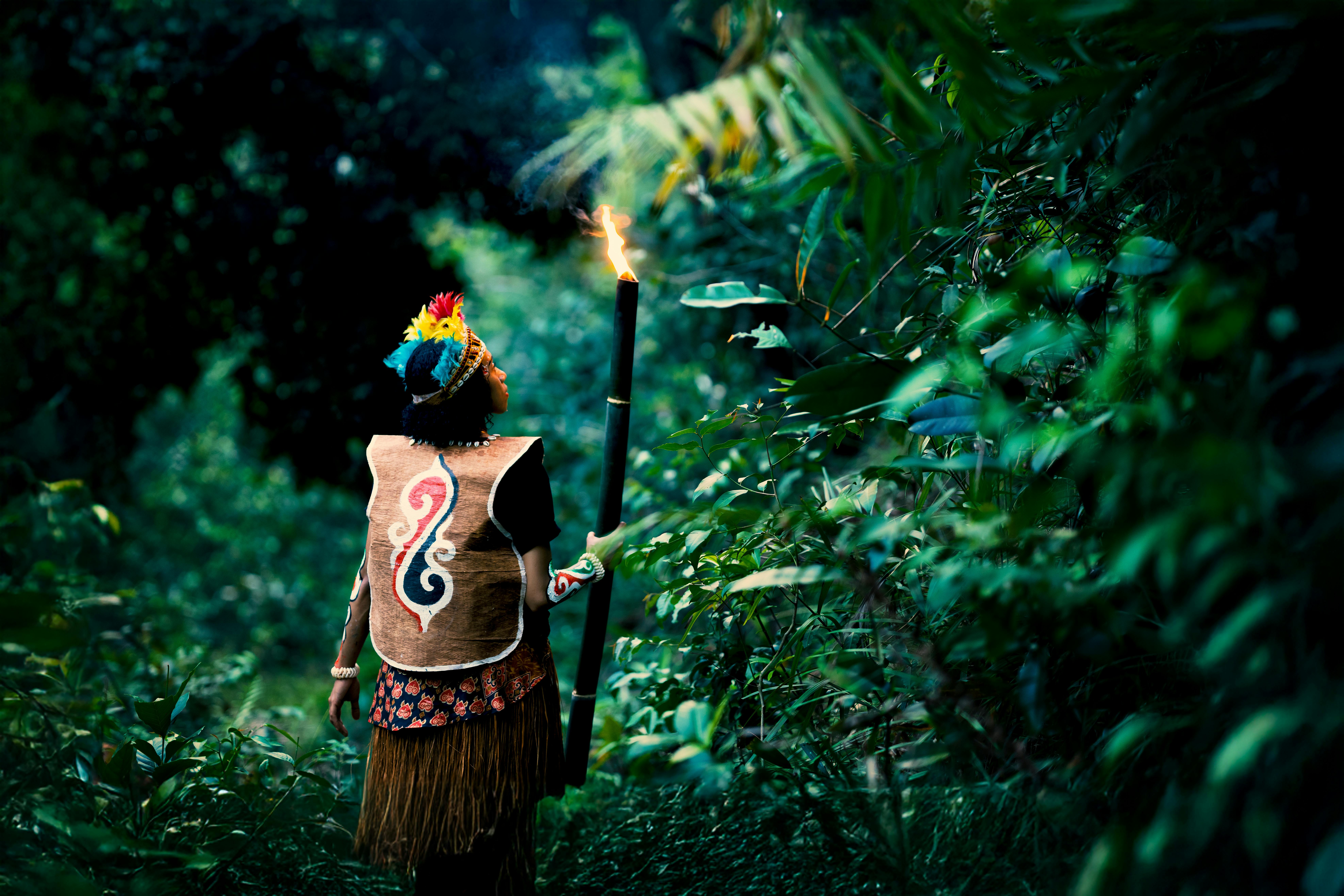 A person in traditional attire holding a torch in a Papua jungle, Jayapura, Indonesia.