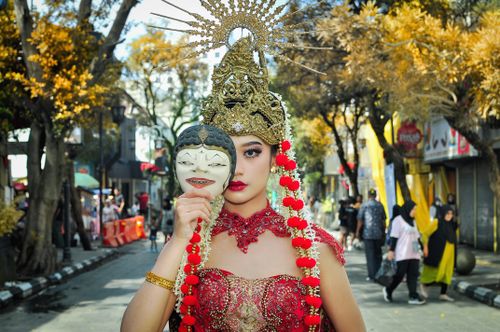 Free Woman in vibrant traditional attire holding a mask in a lively street scene. Stock Photo