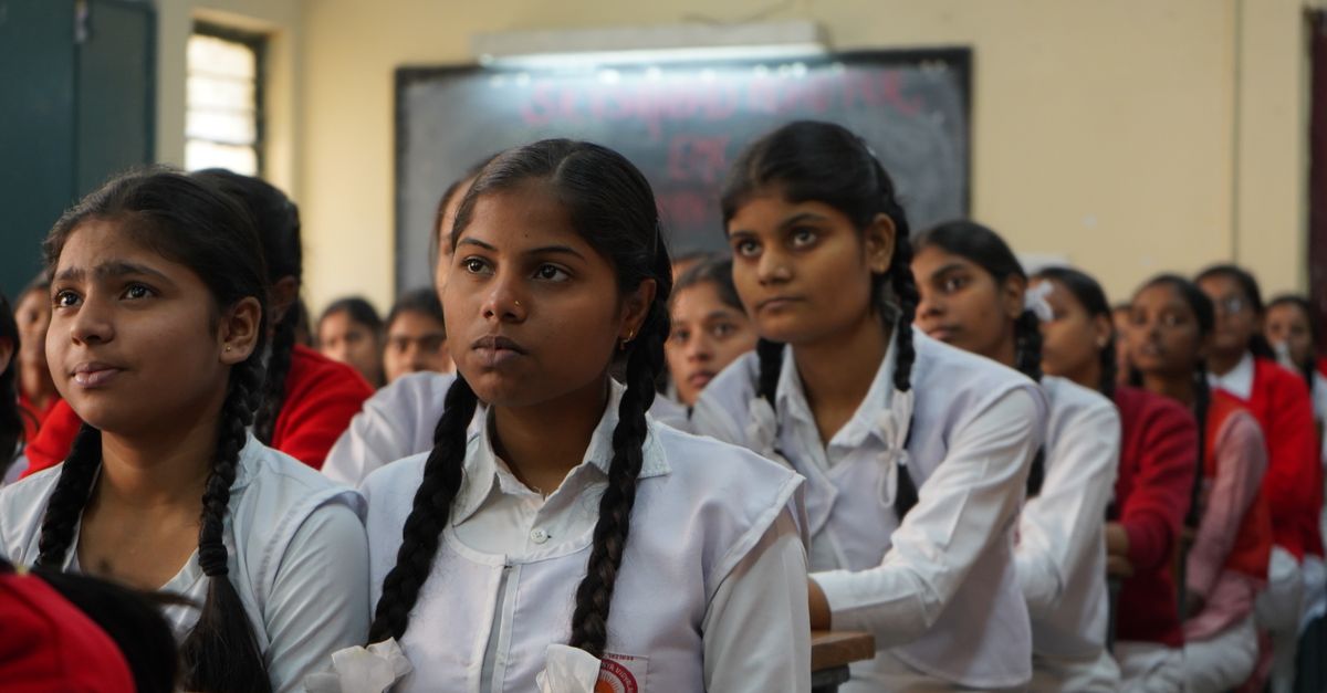 Group of Indian schoolgirls attentively listening in their classroom wearing uniforms.