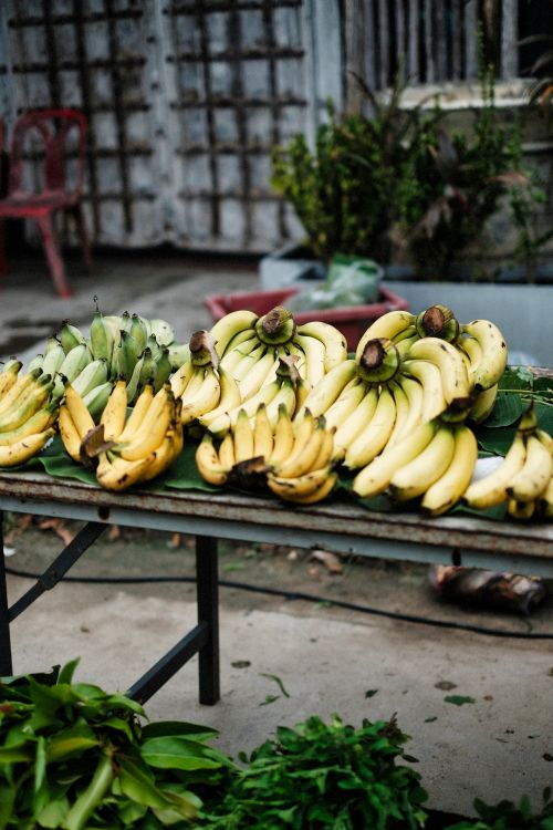 Free Variety of ripe and green bananas arranged on table in an outdoor market setting. Stock Photo