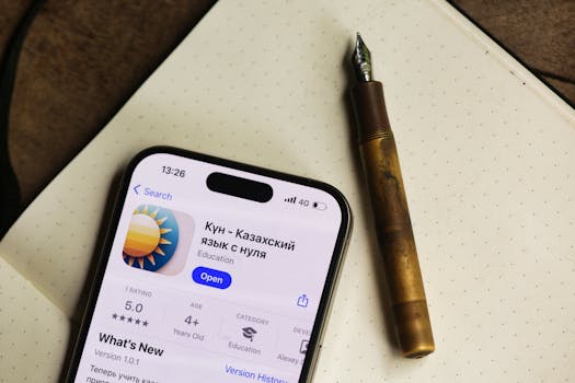 Smartphone displaying Kazakh language app next to a fountain pen on a notebook.