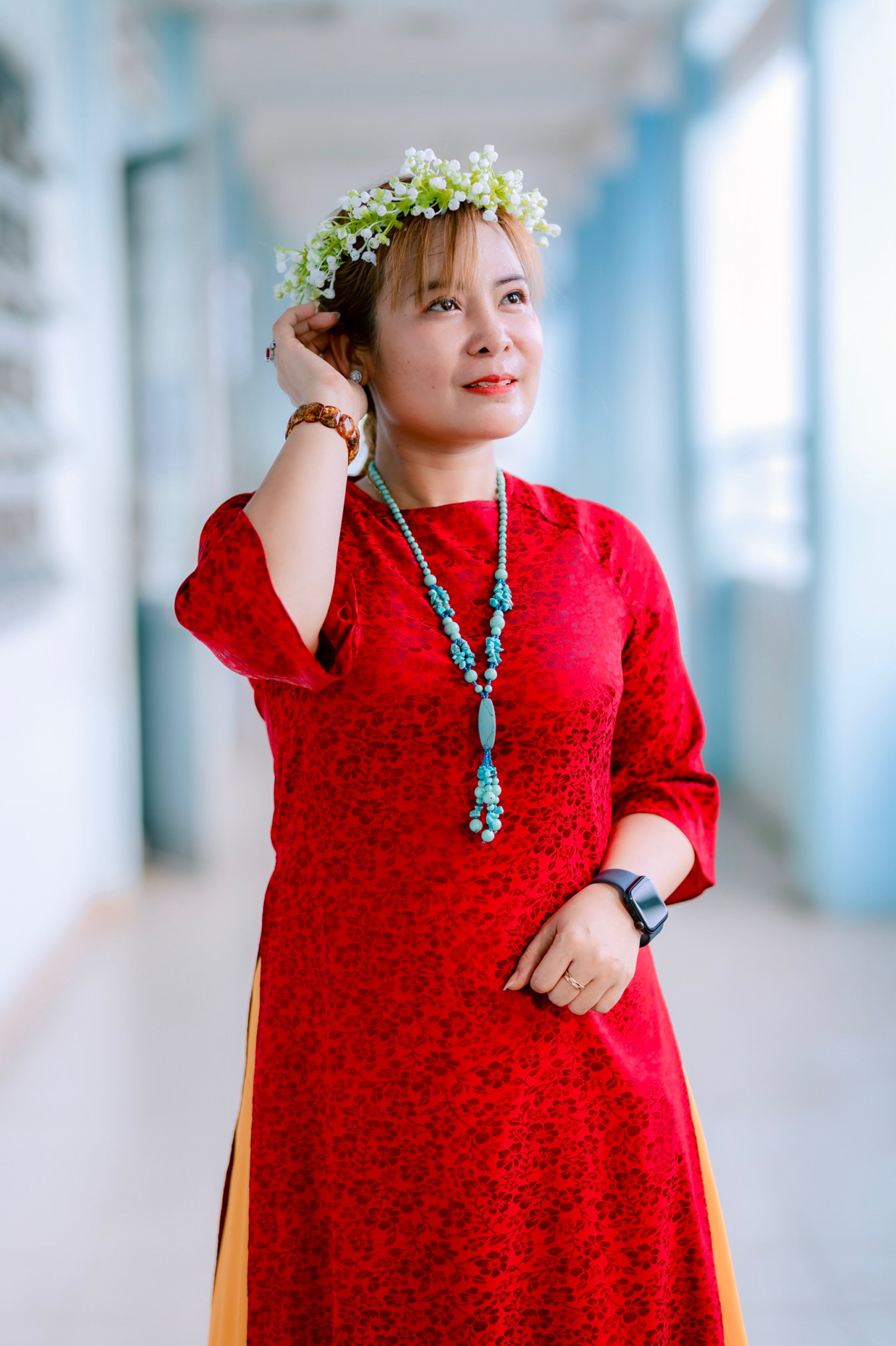 Woman wearing a traditional red dress and floral crown, indoors setting.