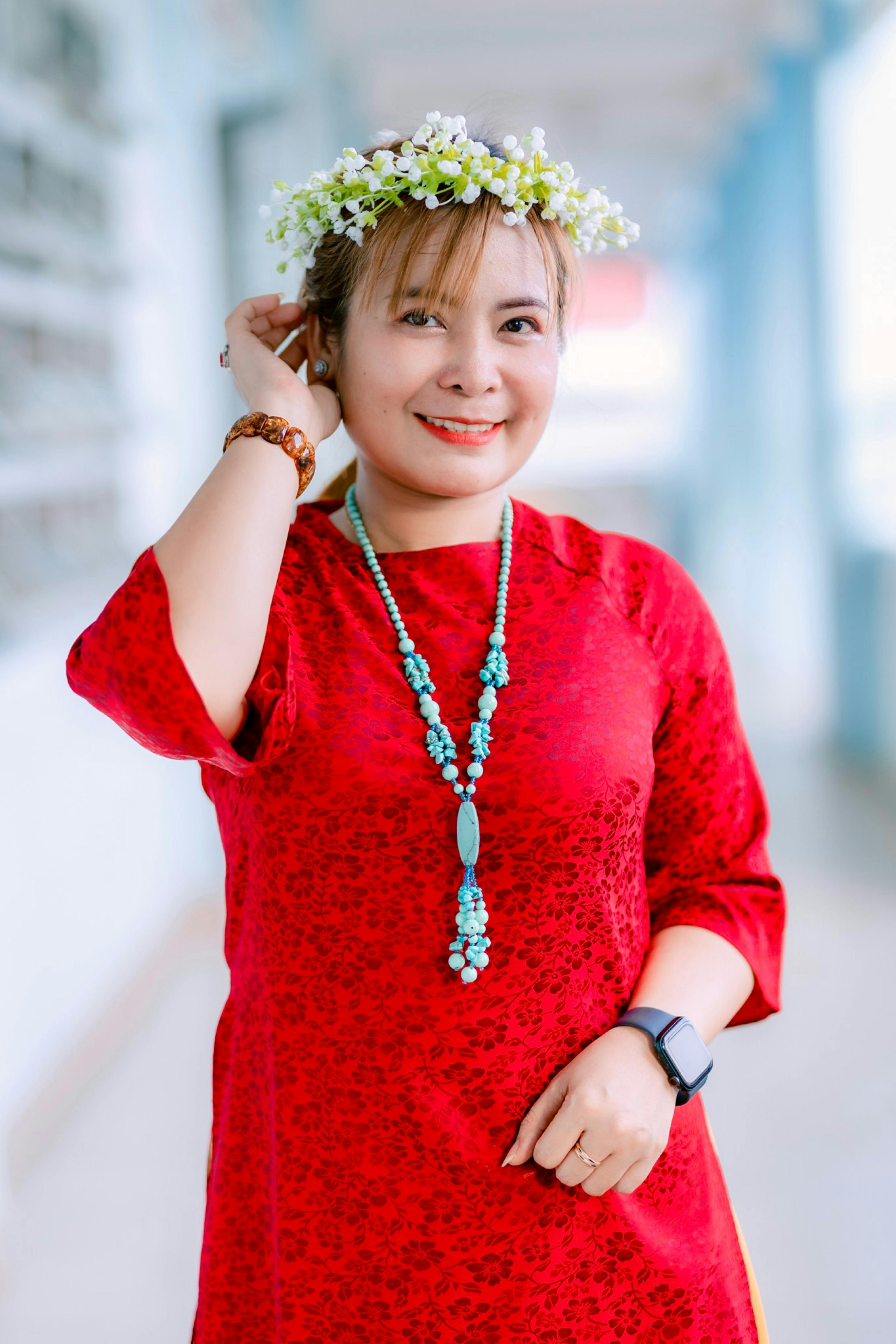 Cheerful woman wearing red dress, floral crown, and turquoise necklace indoors.