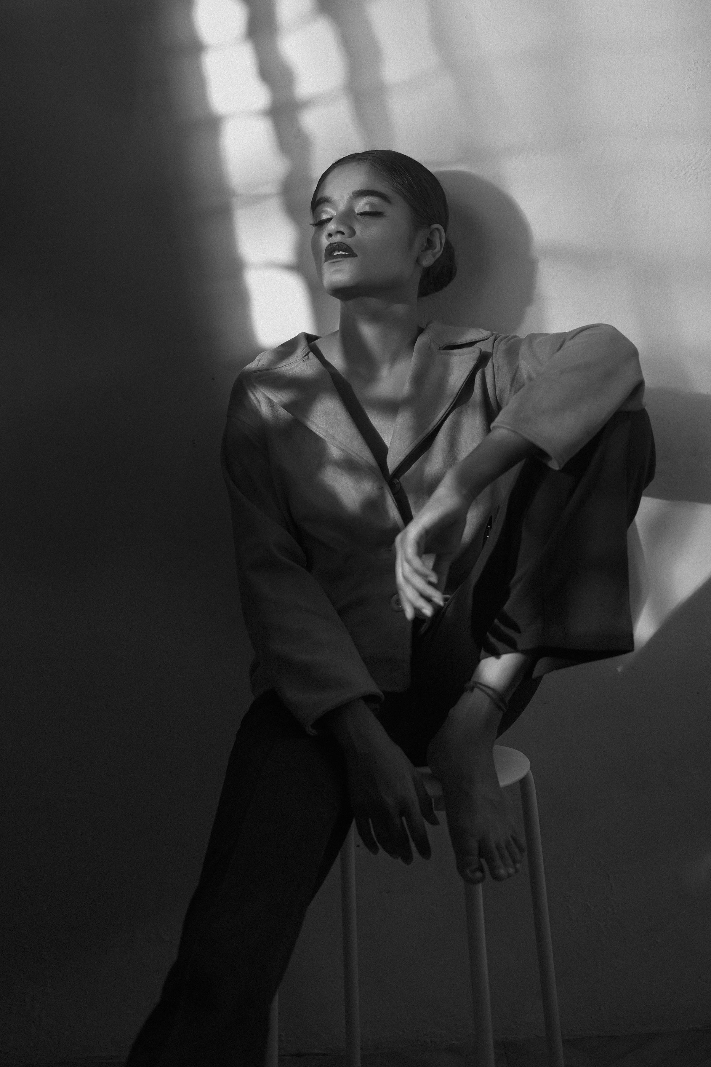 Gratis Elegant sort-hvidt portræt af en model, der sidder i skygge, og som fremviser kunstnerisk udtryk og stemningsfuld belysning. Lagerfoto