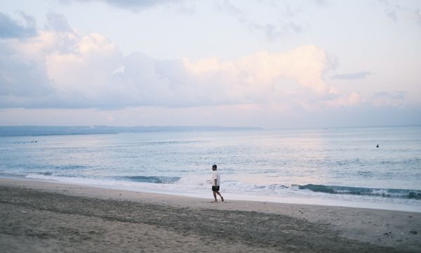 Solitary walk on a tranquil Bali beach at sunset, capturing serenity and natural beauty.