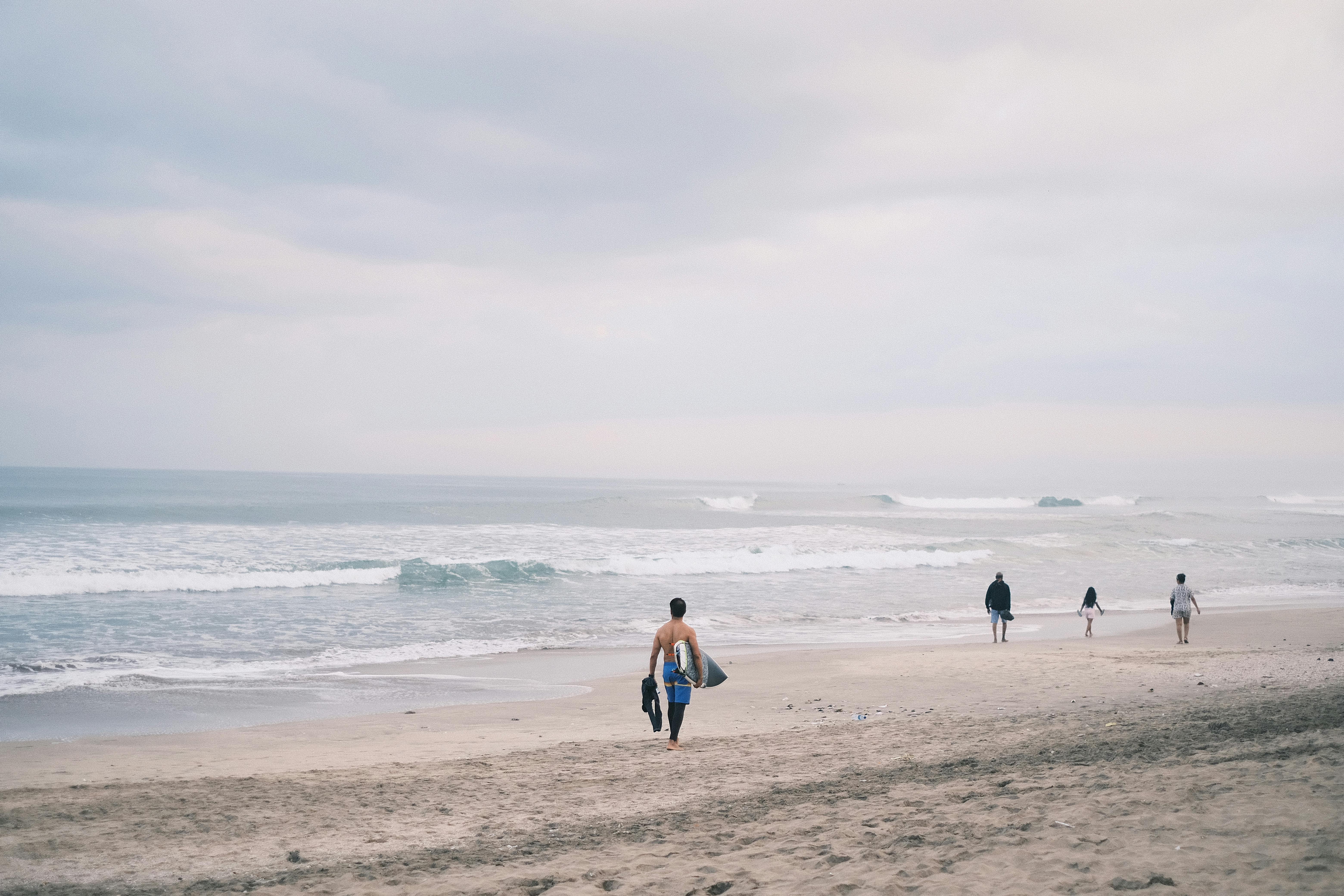 A peaceful beach scene in Bali, Indonesia, with surfers heading to the waves under a cloudy sky.