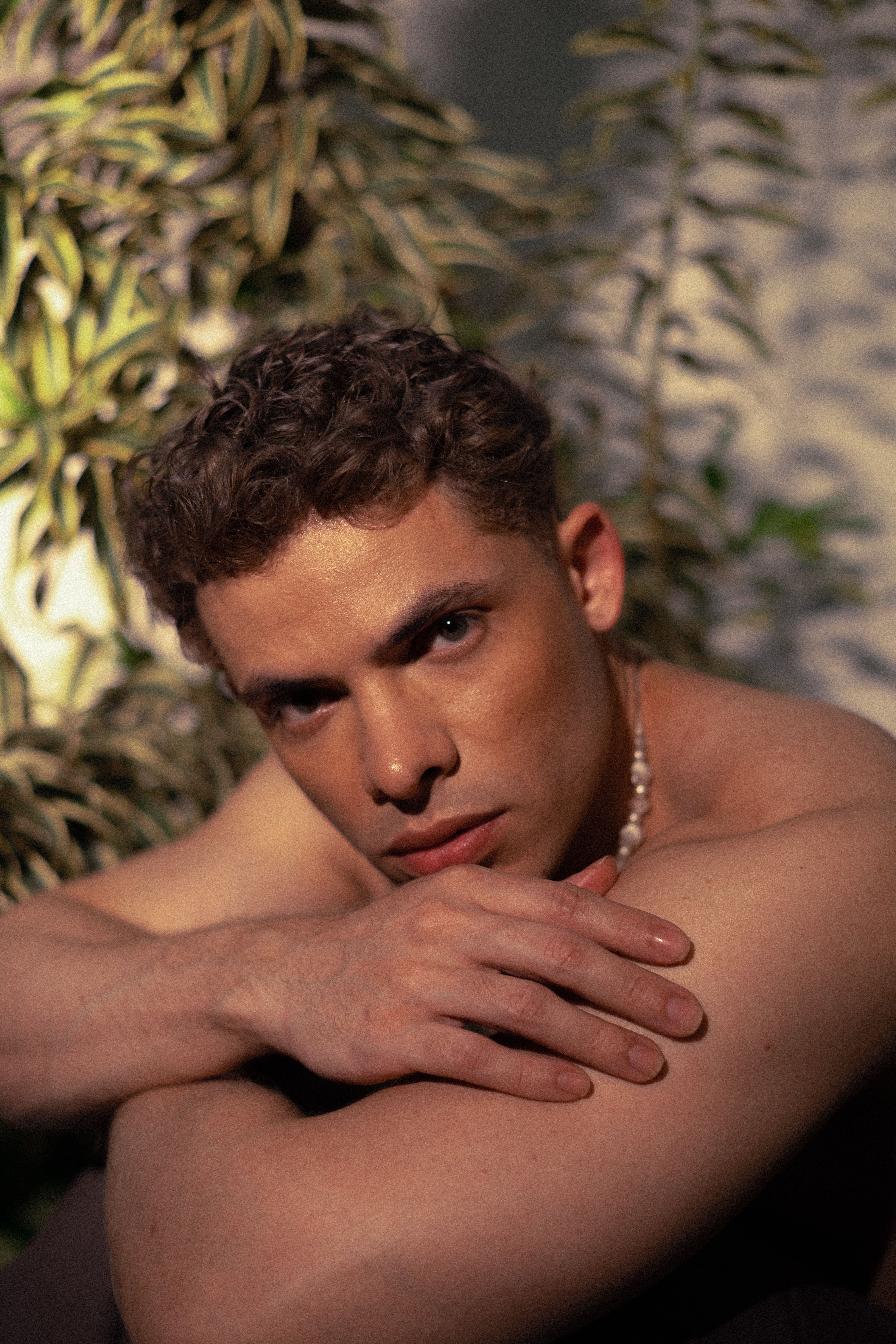 A thoughtful adult man poses against foliage in soft daylight.