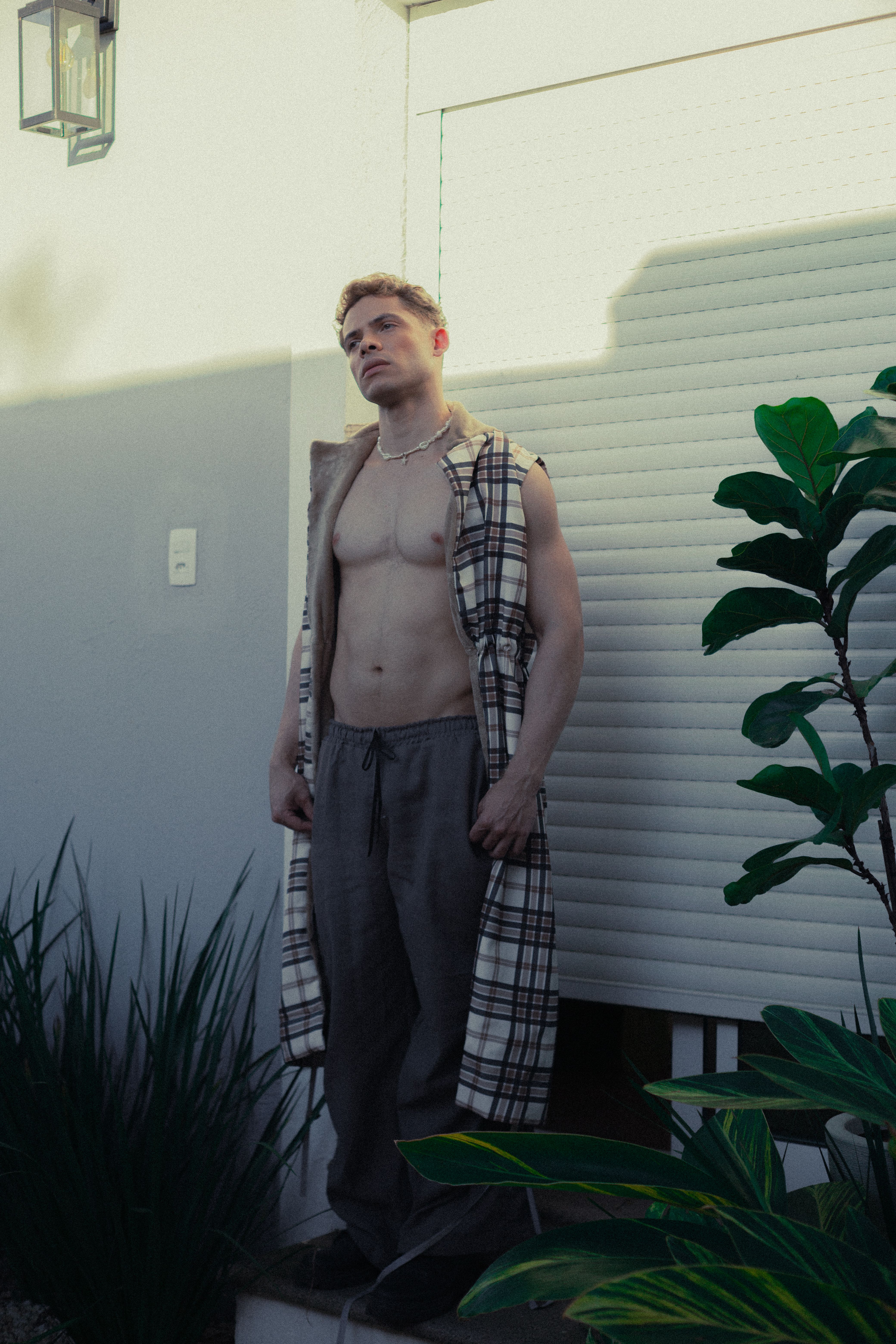 Relaxed portrait of a shirtless young man in a sunlit garden, São Paulo.