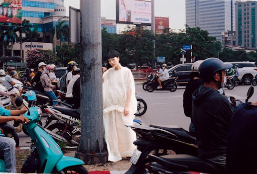 A model in a white dress poses amidst busy city traffic, creating a striking contrast.