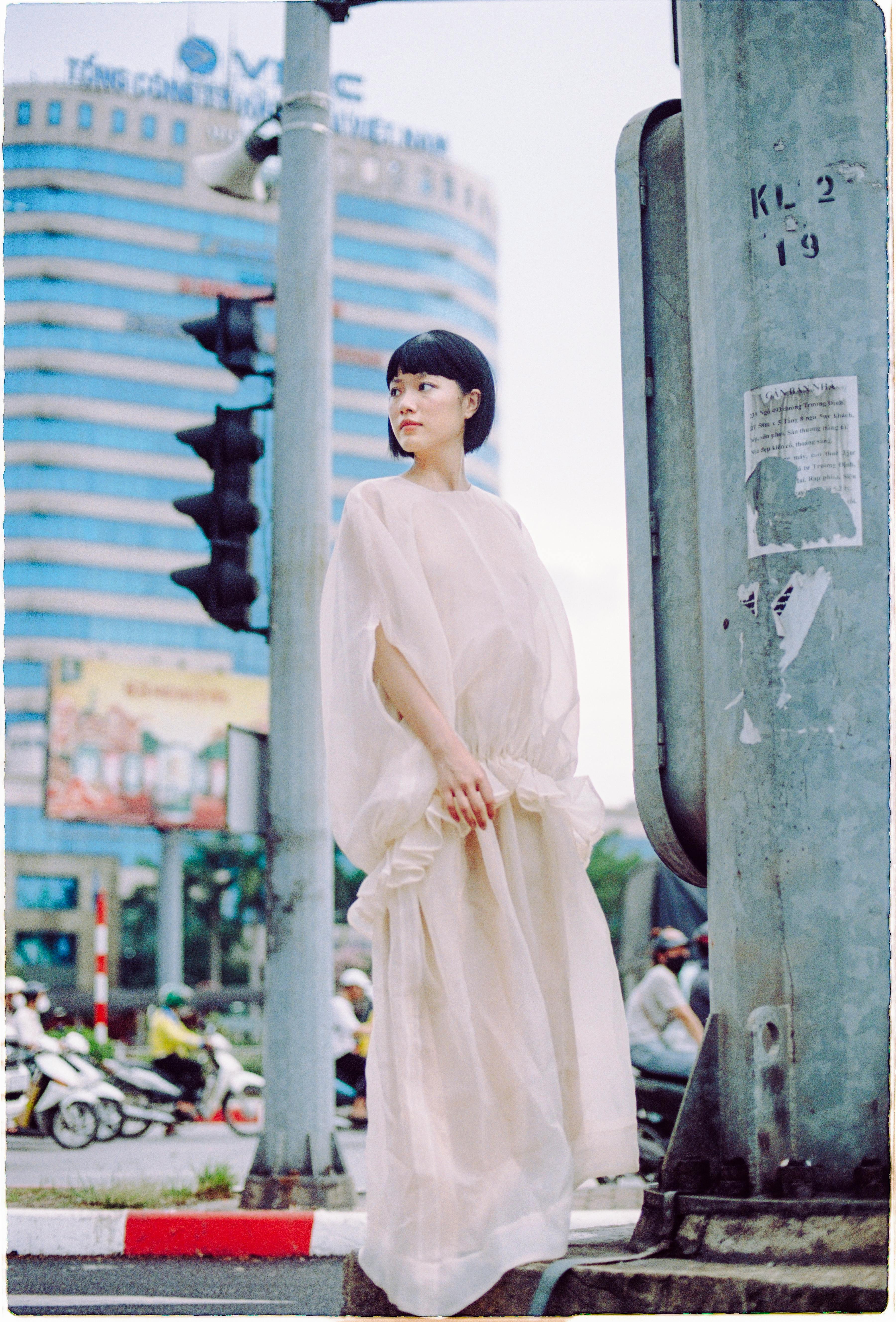 Stylish woman poses in a flowing sheer dress at a busy city intersection.