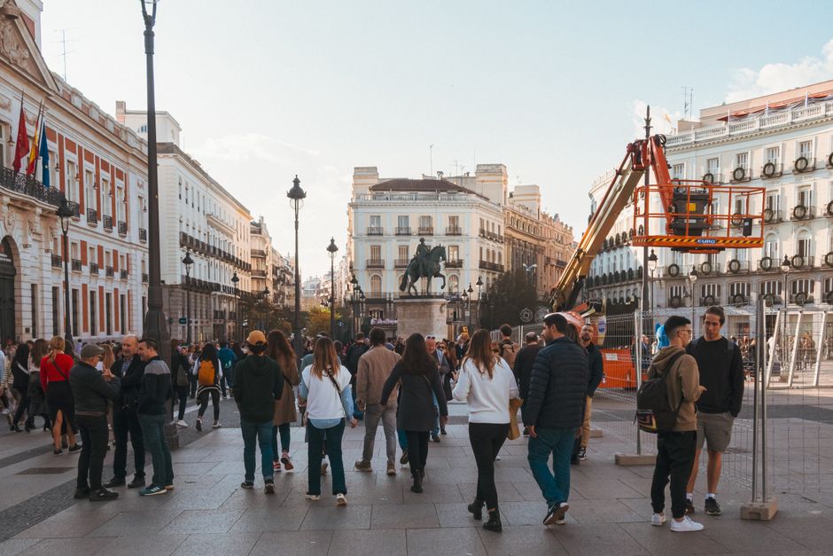 Plaza concurrida de la ciudad de Madrid con gente caminando y arquitectura histórica al fondo.