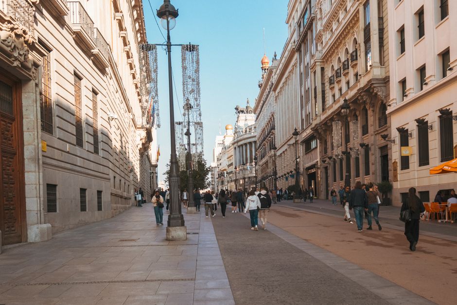 Gente caminando por una vibrante calle europea bordeada de edificios históricos en un día soleado.