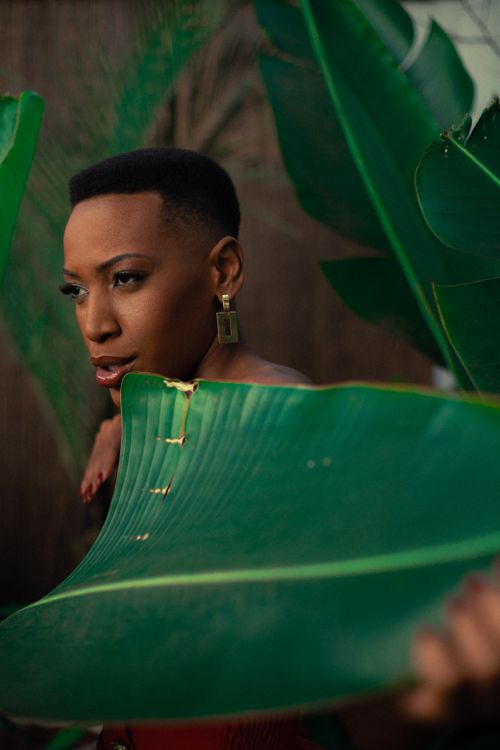 Free Portrait of a stylish woman with vibrant earrings surrounded by lush green leaves. Stock Photo